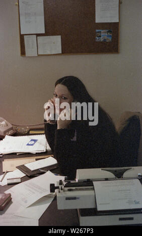 1970s, historical, a young female secretary or office worker, late twenties in age, speaking on the telephone at her desk, with paperwork and typewriter. Stock Photo