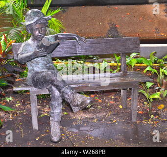 A boy sitting on a bench reading a book bronze statue in the garden of the Pantip Suites hotel in Bangkok Thailand Stock Photo