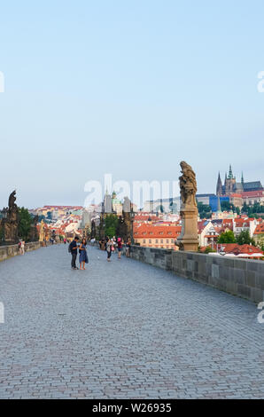 Prague, Czech Republic - June 27th 2019: Tourists walking on beautiful Charles Bridge in the center of Czech capital. Photo from early morning in sunrise light. Gothic landmark, statues. History. Stock Photo