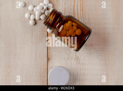 Glass and plastic bottles of medicine. Blue tablets and colored medical capsules on wooden table Stock Photo