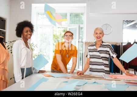 Joyful people. Team of happy tailors standing in a workshop smiling while looking in front of them Stock Photo