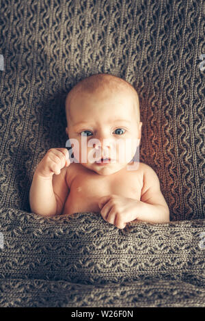 Funny portrait of a full face baby lying in a crib, hand raised up. Voting, elections. Stock Photo