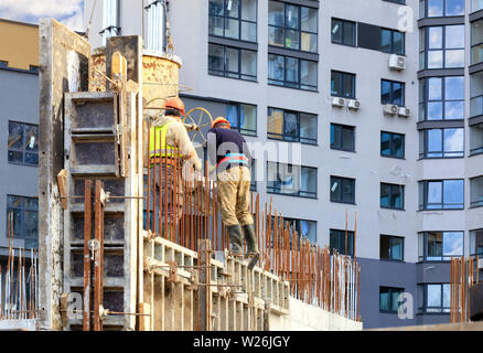 Workers poured concrete in the formwork of the walls on the construction of the new house against the background of a modern residential building. Stock Photo