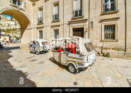 Tourists and guides use three wheel cars to travel through the ancient city of Matera, Italy, an Unesco World Heritage Site. Stock Photo