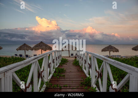Beautiful view of a wooden path leading to the sandy beach on the Caribbean Sea in Cuba during a cloudy and rainy morning sunrise. Stock Photo