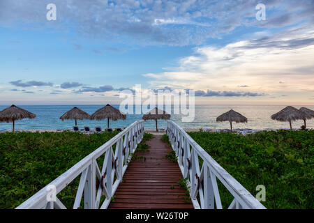 Beautiful view of a wooden path leading to the sandy beach on the Caribbean Sea in Cuba during a cloudy sunset. Stock Photo