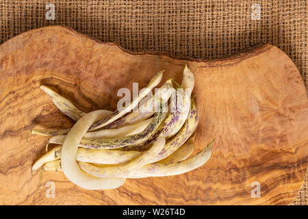 Organic flat yellow wax beans pile on jute fabric and olive wood cut board background. Stock Photo