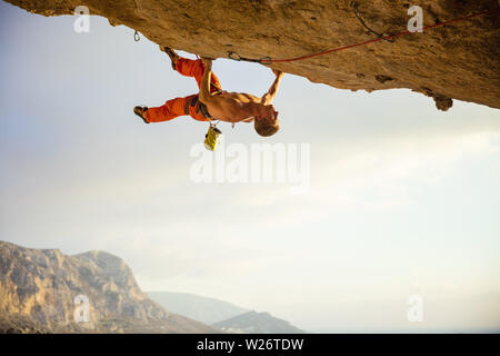Caucasian young man climbing on ledge in cave before sunset Stock Photo