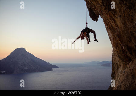 Young female rock climber hanging on rope while being lowered down at sunset Stock Photo