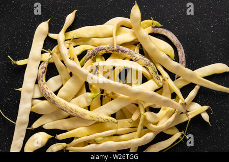 Organic flat yellow wax beans pile on black cut board. Stock Photo