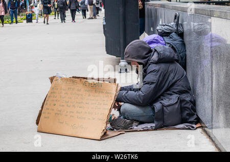 USA, Chicago, Illinois. May 9, 2019. Homeless veteran sitting on the roadside holding a cardboard sign, asking for help, downtown Stock Photo