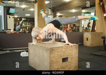 Young blonde female gymnast doing handstand in gym, copyspace Stock Photo