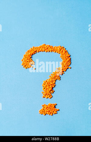 Flat lay question mark made from small orange lentils over blue background, copy space. Stock Photo