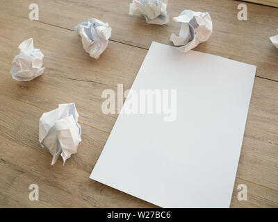 Writing concept - crumpled up paper wads with a sheet of white paper. Stock Photo