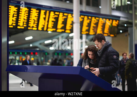 London, UK - February, 2019. A young couple seeking information at a desk inside London Bridge Rail Station, with timetables on the background. Stock Photo
