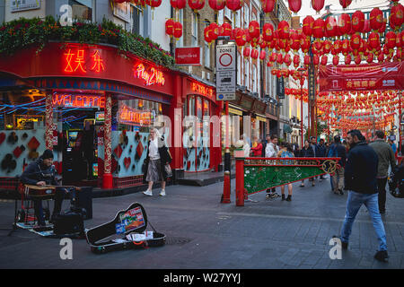 London, UK - April, 2019. Street musician playing a guitar during a performance in Chinatown. Stock Photo