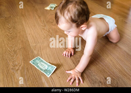 Baby reaching some dollar bills, wasted family savings concept Stock Photo