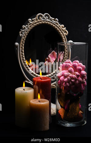 Vintage Oval Desk Mirror with white frame, potpourri, and candles reflecting in mirror on black background Stock Photo