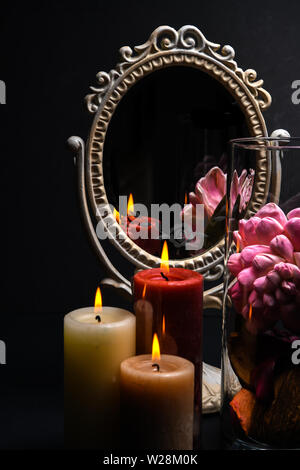 Vintage Oval Desk Mirror with white frame, potpourri, and candles reflecting in mirror on black background Stock Photo