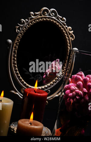 Vintage Oval Desk Mirror with white frame, potpourri, and candles reflecting in mirror on black background Stock Photo
