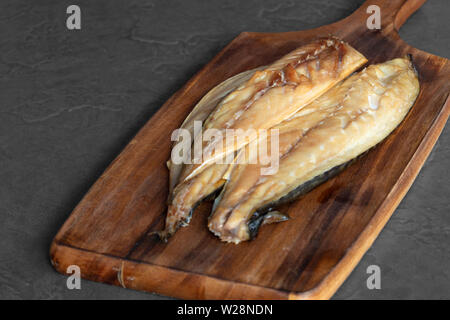 Raw smoked mackerel fillets on a rustic wooden chopping board.  With a grey tile background Stock Photo