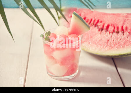 Fruit salad with melon and watermelon balls in glass and pice of watermelon under the palm leaf on the white background Stock Photo