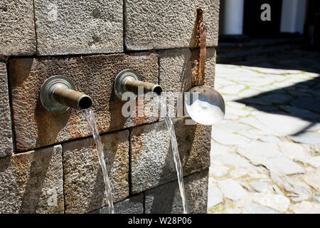 Stone fountain with two iron spouts. The metal spouts of the old old stone fountain Stock Photo