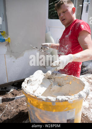 plasterer in red shirt works on white plaster of old house during insulation work Stock Photo