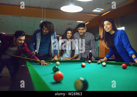 Friends play billiards in bar. A group of young people playing fun billiards. Stock Photo