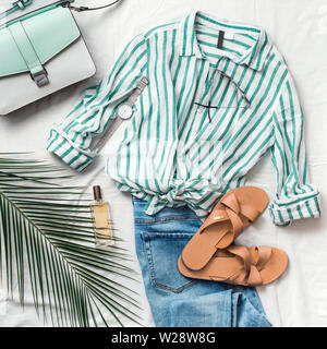 Feminine summer fashion composition: striped blouse, slippers, bag, sunglasses, watch, perfume, jeans, palm leaf on white background. Flat lay, top view clothes. Female fashion blog or social media Stock Photo