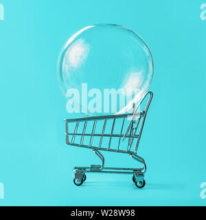 Shopping cart with soap bubble on bright blue background. Ephemeral happiness from shopping, shopaholism, consumerism concept. Shopping concept, minimalist creative layout Stock Photo