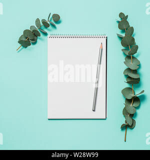 Blank notebook, pencil and eucalyptus on blue background. Empty notebook paper and eucalyptus branch on pastel blue background with copy space for text or design. Flat lay, top view, copyspace, square Stock Photo