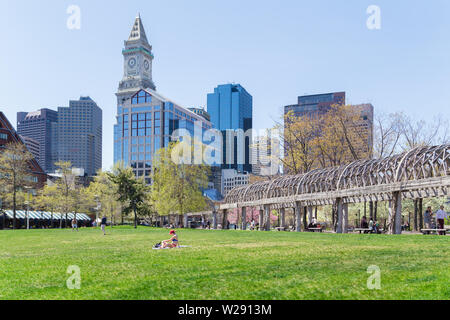 A woman sunbathes on green grass park ground at Christopher Columbus Waterfront Park located by the harbor in downtown Boston, Massachusetts, USA. Stock Photo