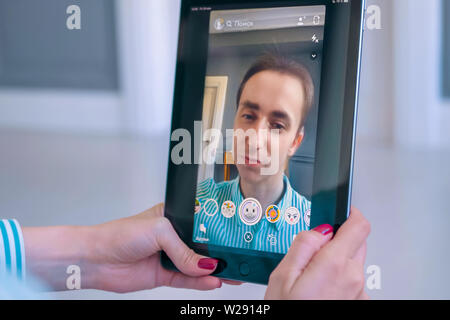 Woman using Snapchat multimedia messaging app with face mask on tablet Stock Photo