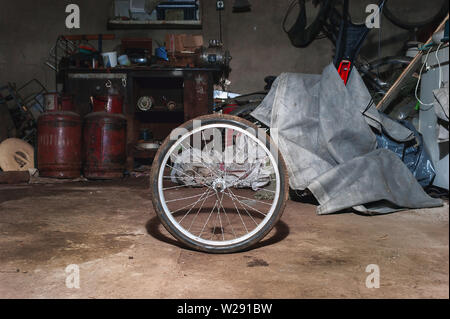 Dirty Bicycle Wheel on the Floor of a Messy Home Garage with Equipment, Workbench, Tools and Cloth in Background. Stock Photo