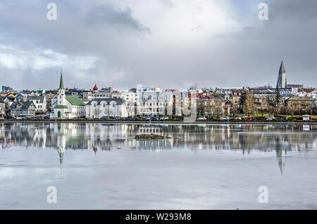 Reykjavik, Iceland, February 23, 2019: the eastern bank of Lake Tjornin with Frikirkja and Hallgrimskirkja churches reflect in the ice under a dramati Stock Photo