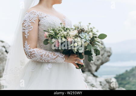 A bride in a white dress is holding a beautiful wedding bouquet. Fresh flowers, including peony roses. Wedding celebration. Stock Photo