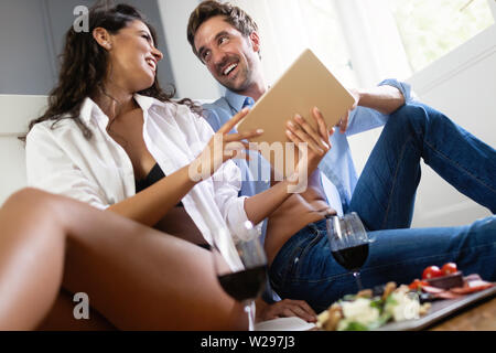 Romantic young couple relaxing together in bedroom,drinking wine and using tablet Stock Photo