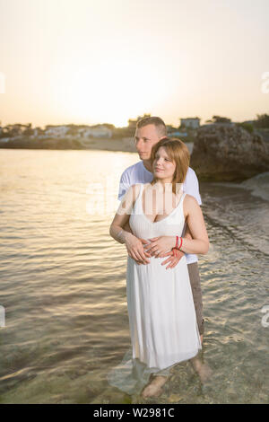 Pregnant woman embracing with her husband on the beach at sunset Stock Photo