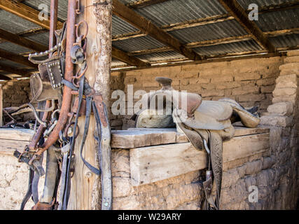 Western Style Bridle And Saddle. Interior of barn with worn and cracked leather riding saddle and a group of horse bridles. Stock Photo