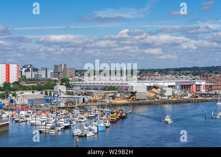 Boats towed along the Itchen river with the St Mary's football stadium in the background, view from Itchen bridge, Southampton, England, UK Stock Photo