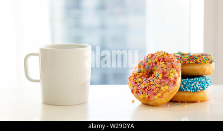 Donuts and coffee for breakfast. Colorful donuts and cup of coffee on white table. Close up view Stock Photo