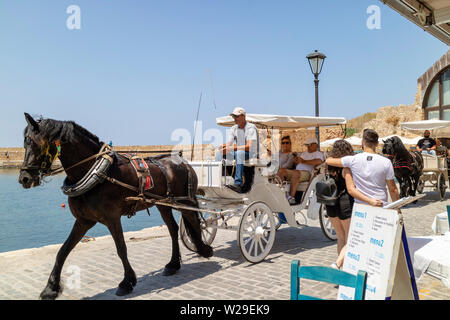 Chania, Crete, Greece. June 2019. Tourists taking a ride in an open carriage around the Old Venetian Harbour in Chania Stock Photo