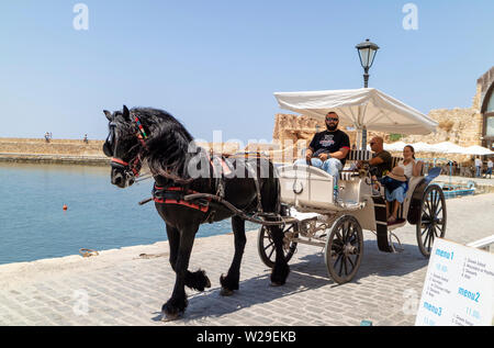 Chania, Crete, Greece. June 2019. Tourists taking a ride in an open carriage around the Old Venetian Harbour in Chania Stock Photo