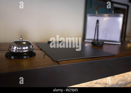 Service bell locating at reception. Silver call bell on table, receptionists on background. Stock Photo