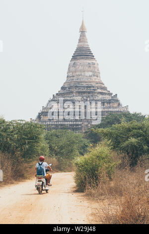 Man riding electric scooter along dirt road towards temples and pagodas of ancient Bagan in Myanmar Stock Photo