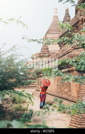 Blonde Caucasian woman with red traditional umbrella stands among the temples and pagodas of ancient Bagan in Myanmar