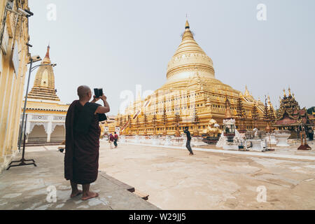 Bagan, Myanmar - March 2019: Burmese Buddhist monk taking picture of Shwezigon Paya golden temple