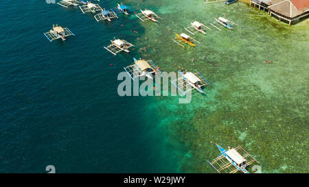 Tourists snorkeling over coral reef with clear blue ocean water, aerial view. Moalboal, Philippines. People swim in the transparent sea between coral reefs. Summer and travel vacation concept. Stock Photo