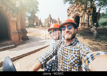 Young Caucasian couple making selfie on a motorbike while driving through temples and pagodas of ancient Bagan in Myanmar. Stock Photo